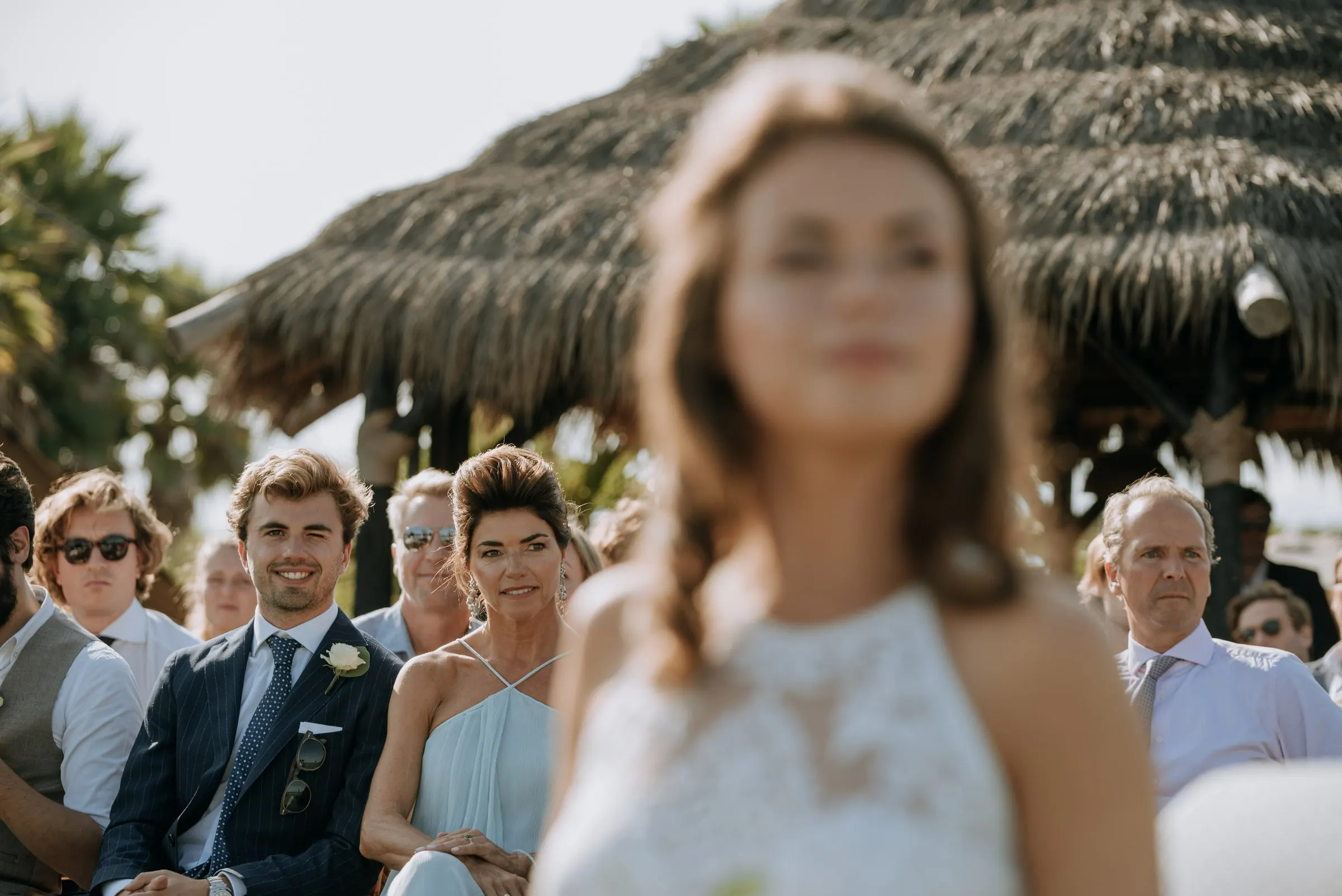 Guests smiling in their seats as the bride passes out of focus in the foreground, Trocadero, Sotogrande