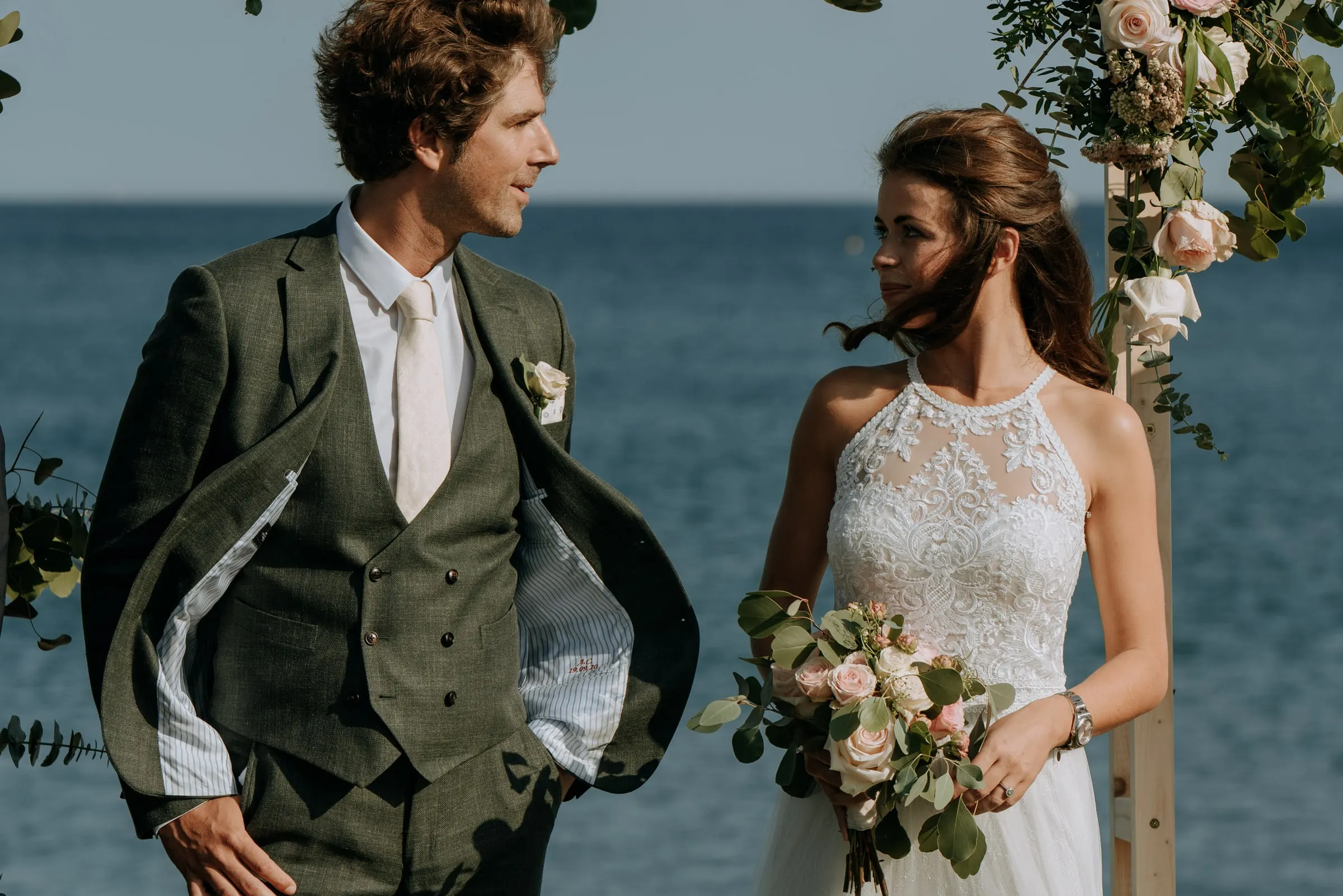 Groom in a green suit and bride holding her bouquet, glancing out to sea, Trocadero, Sotogrande