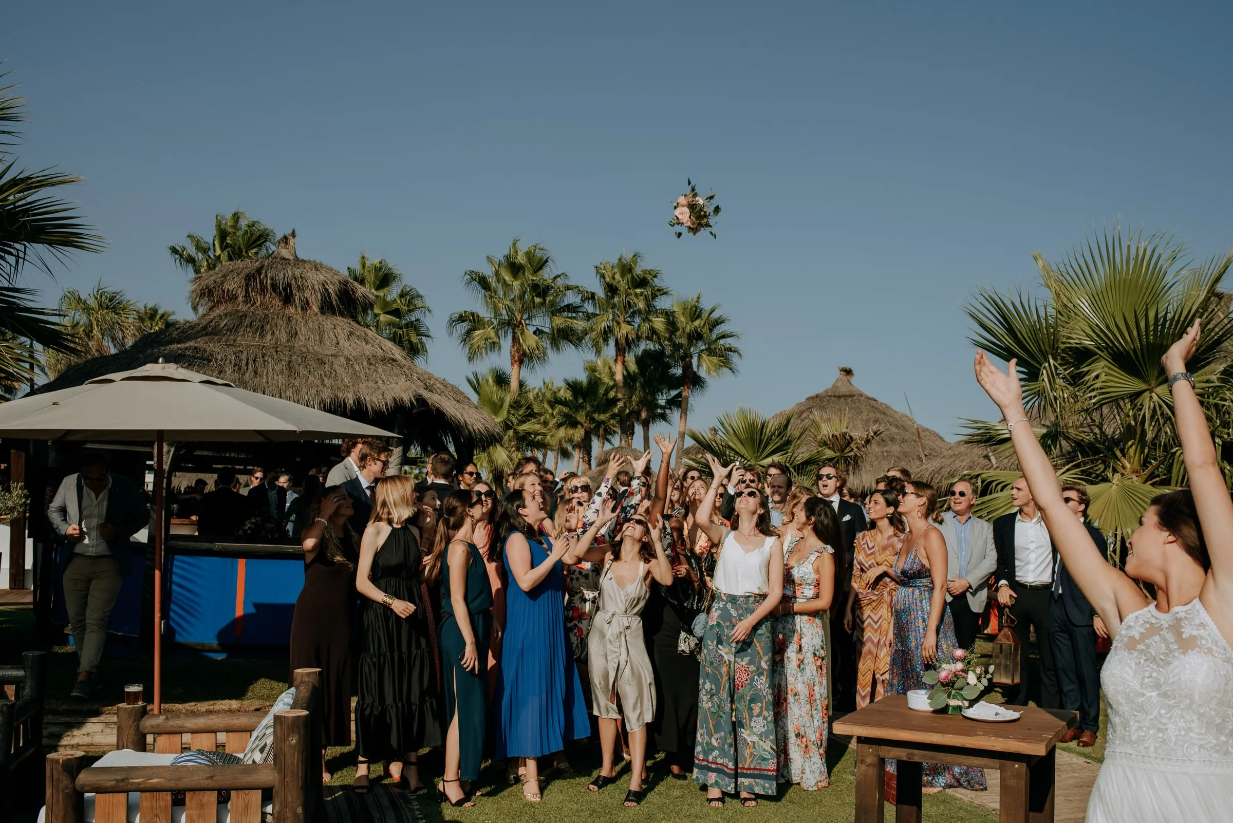The bride tossing her bouquet to a crowd of guests among the palm trees, Trocadero, Sotogrande