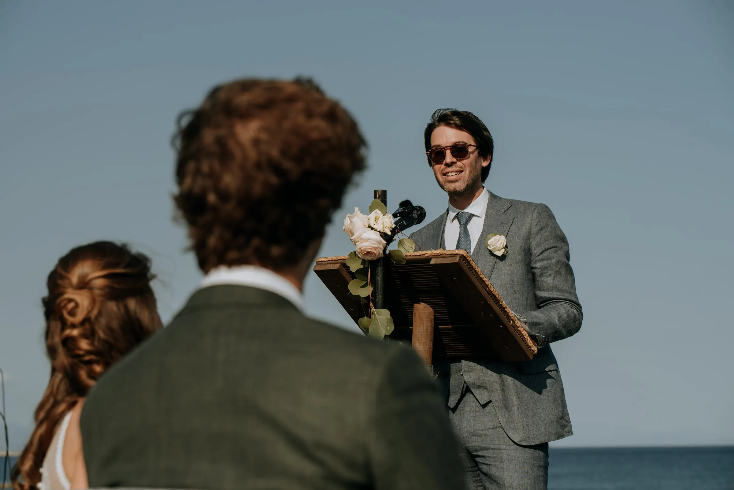 The officiant smiling at the lectern, seen past the couple's shoulders, Trocadero, Sotogrande