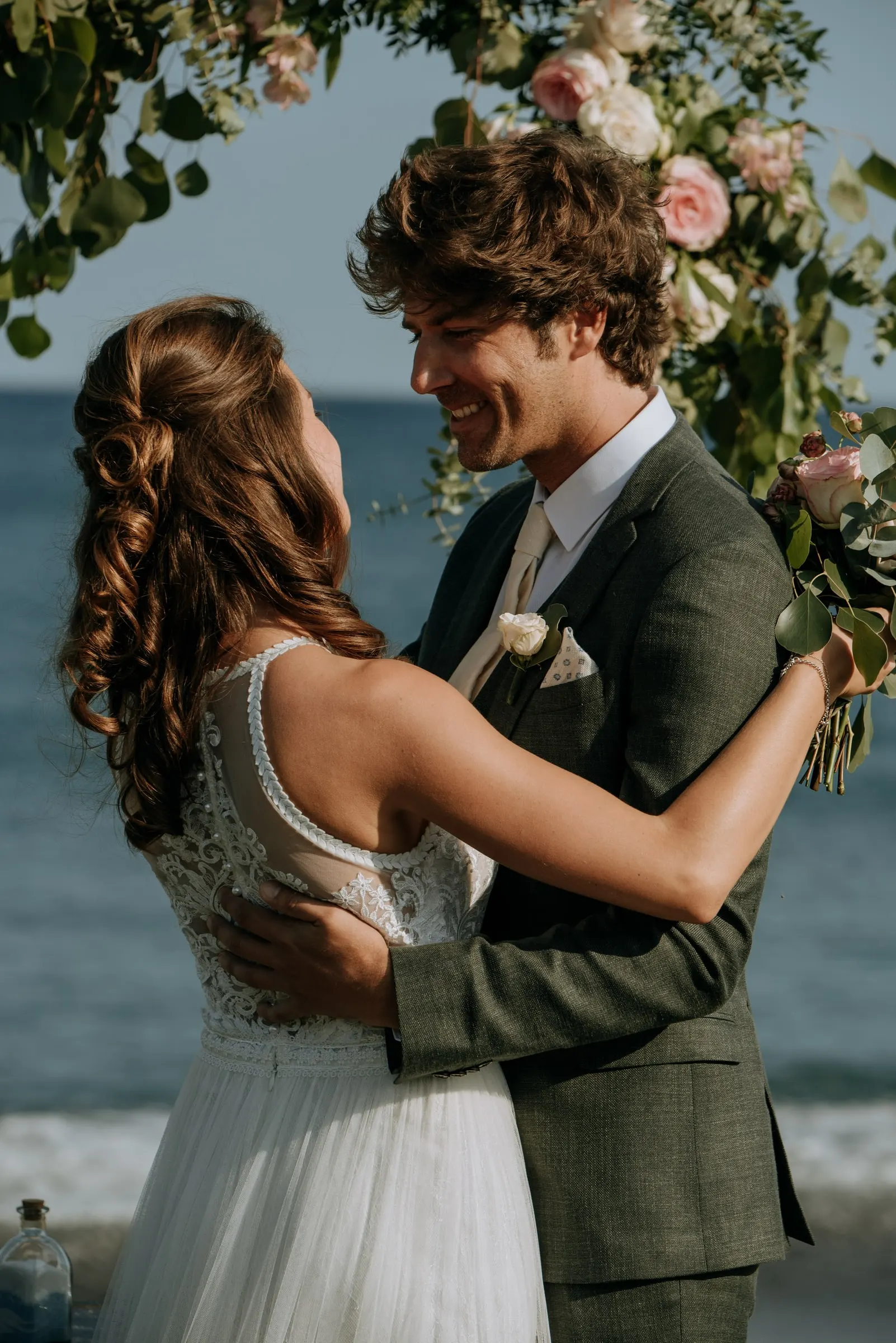 Bride and groom hugging and smiling under the flower arch by the sea, Trocadero, Sotogrande
