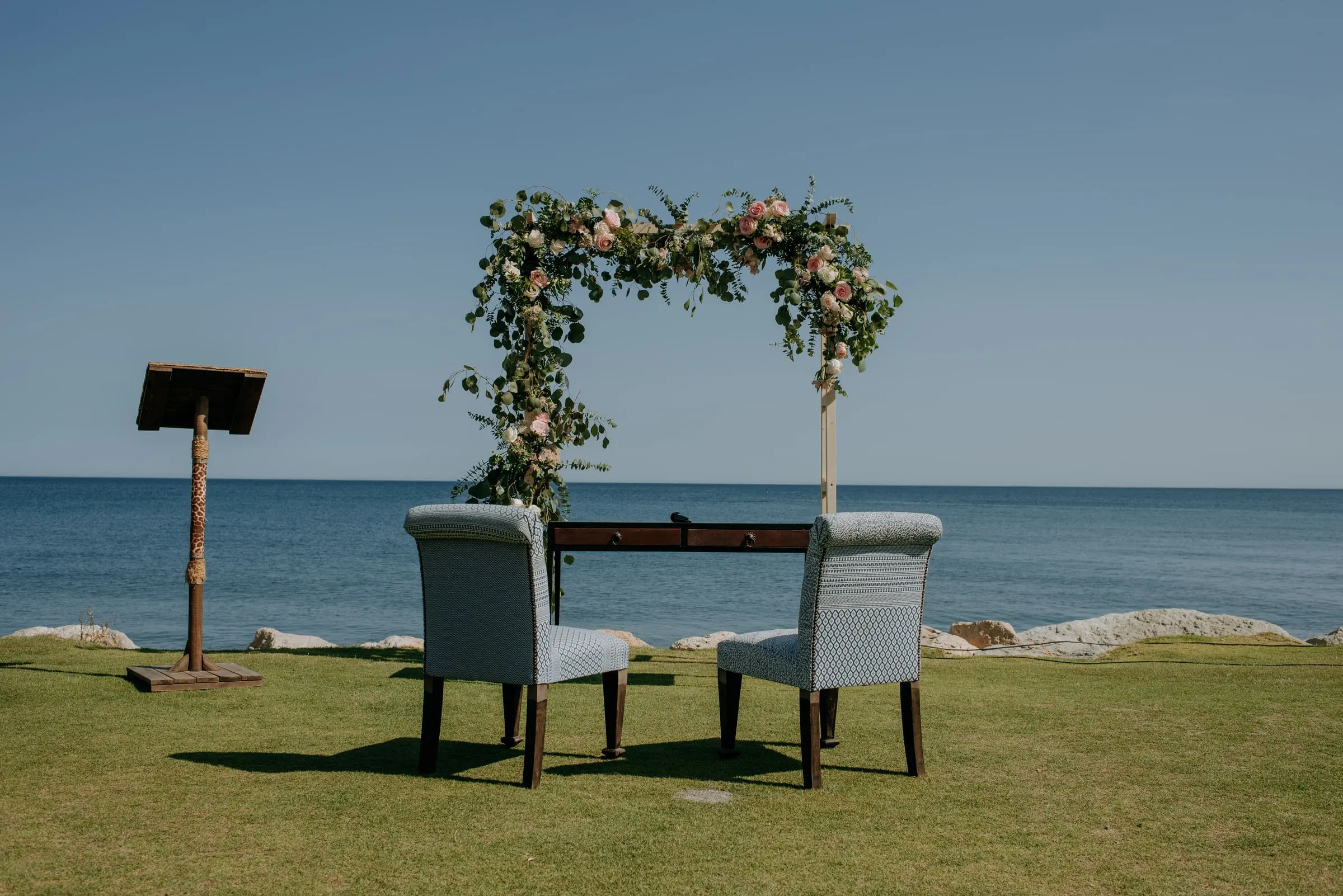 The empty ceremony set-up: flower arch, two armchairs and a lectern by the sea, Trocadero, Sotogrande