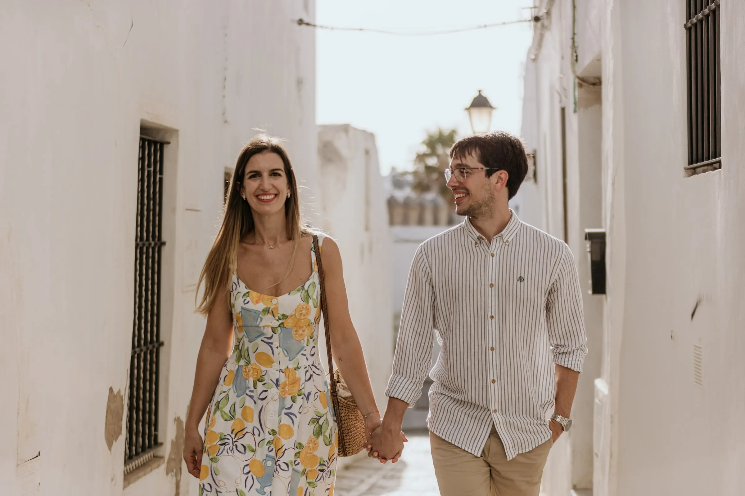 La pareja ríe mientras camina de la mano por una calle blanca y soleada de Andalucía