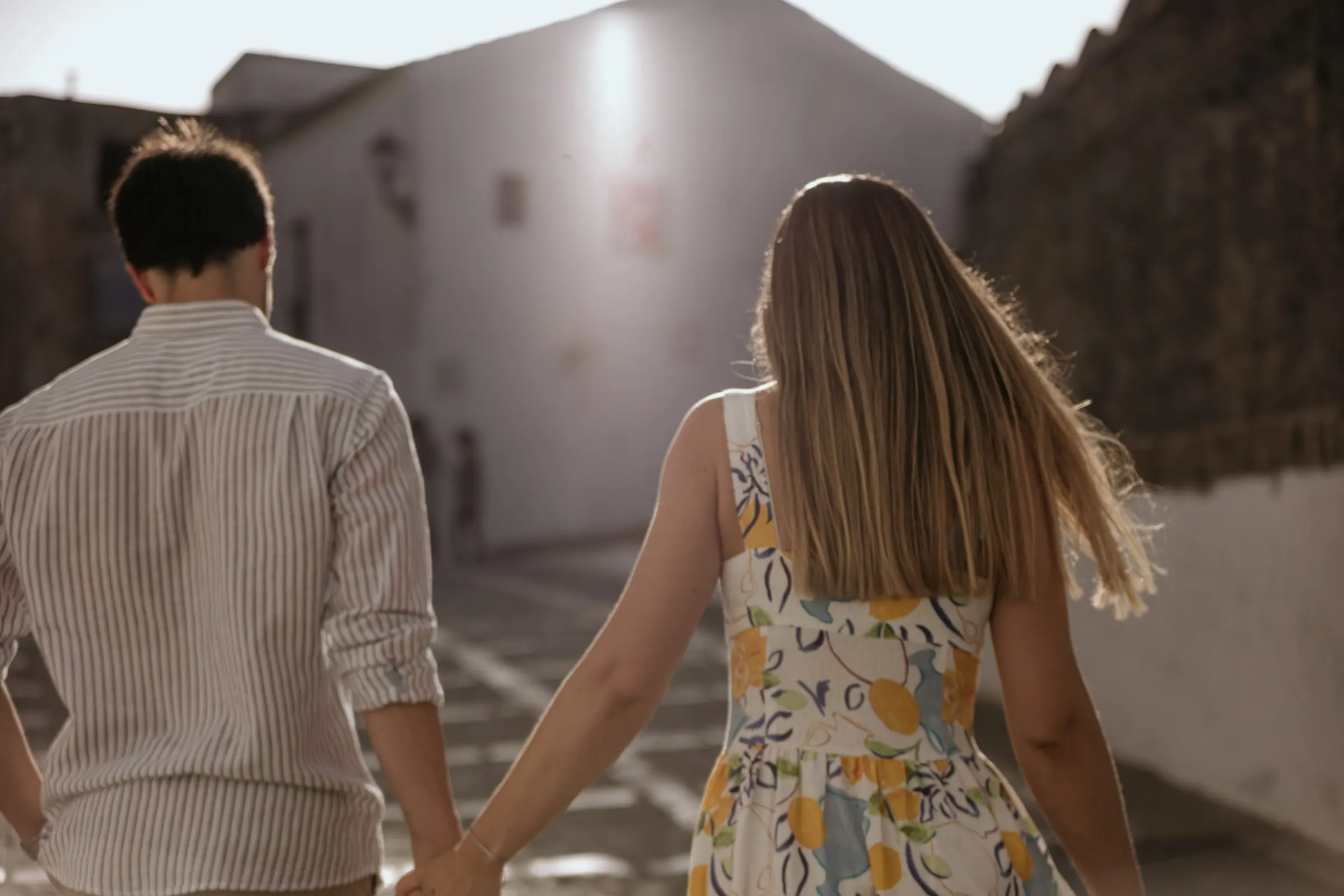 La pareja de espaldas sube de la mano una calle blanca hacia el sol, Vejer