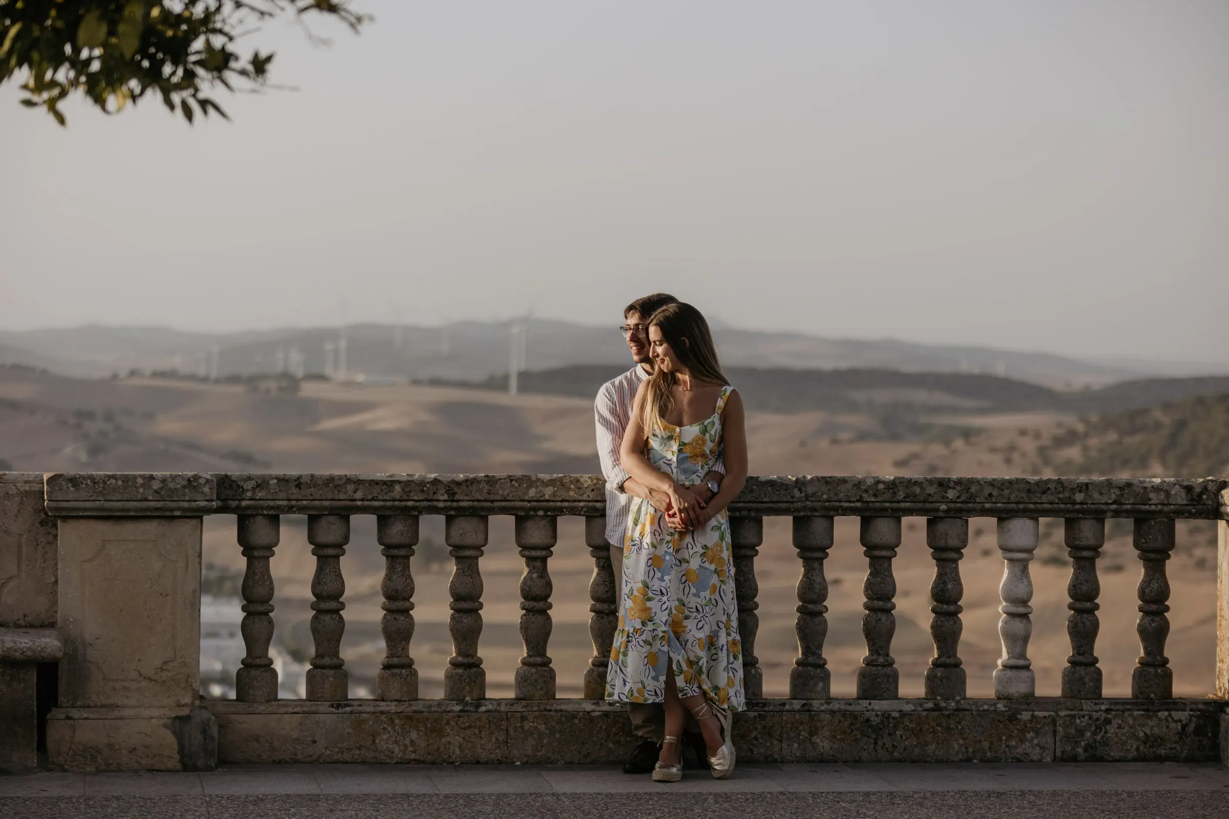 La futura novia apoyada en su prometido sobre una balaustrada de piedra ante las colinas de Cádiz