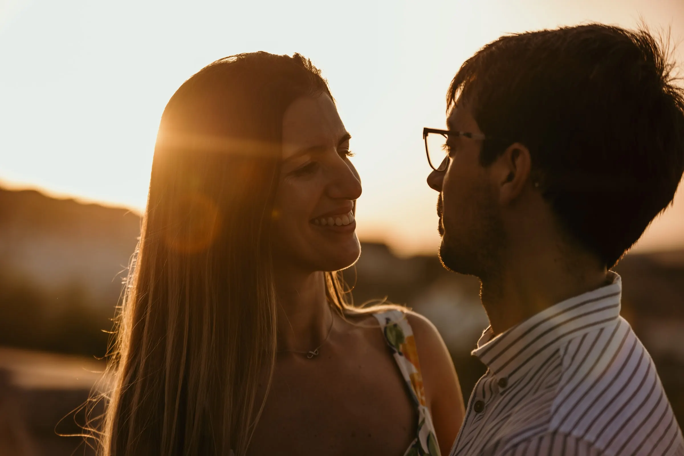 Couple laughing face to face with the setting sun flaring between them, Vejer