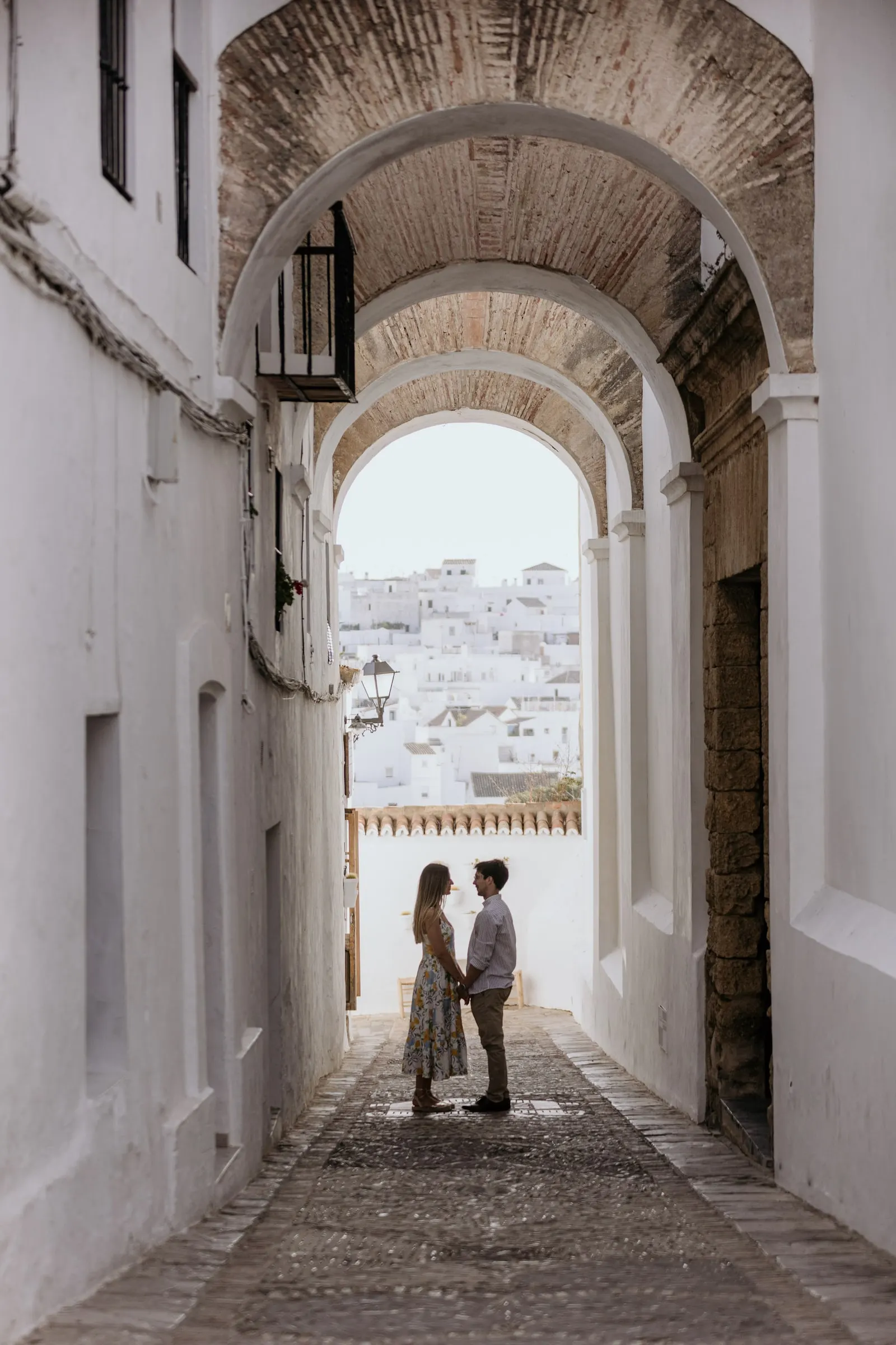 La pareja frente a frente bajo los arcos encalados de un callejón de Vejer, con el pueblo blanco al fondo