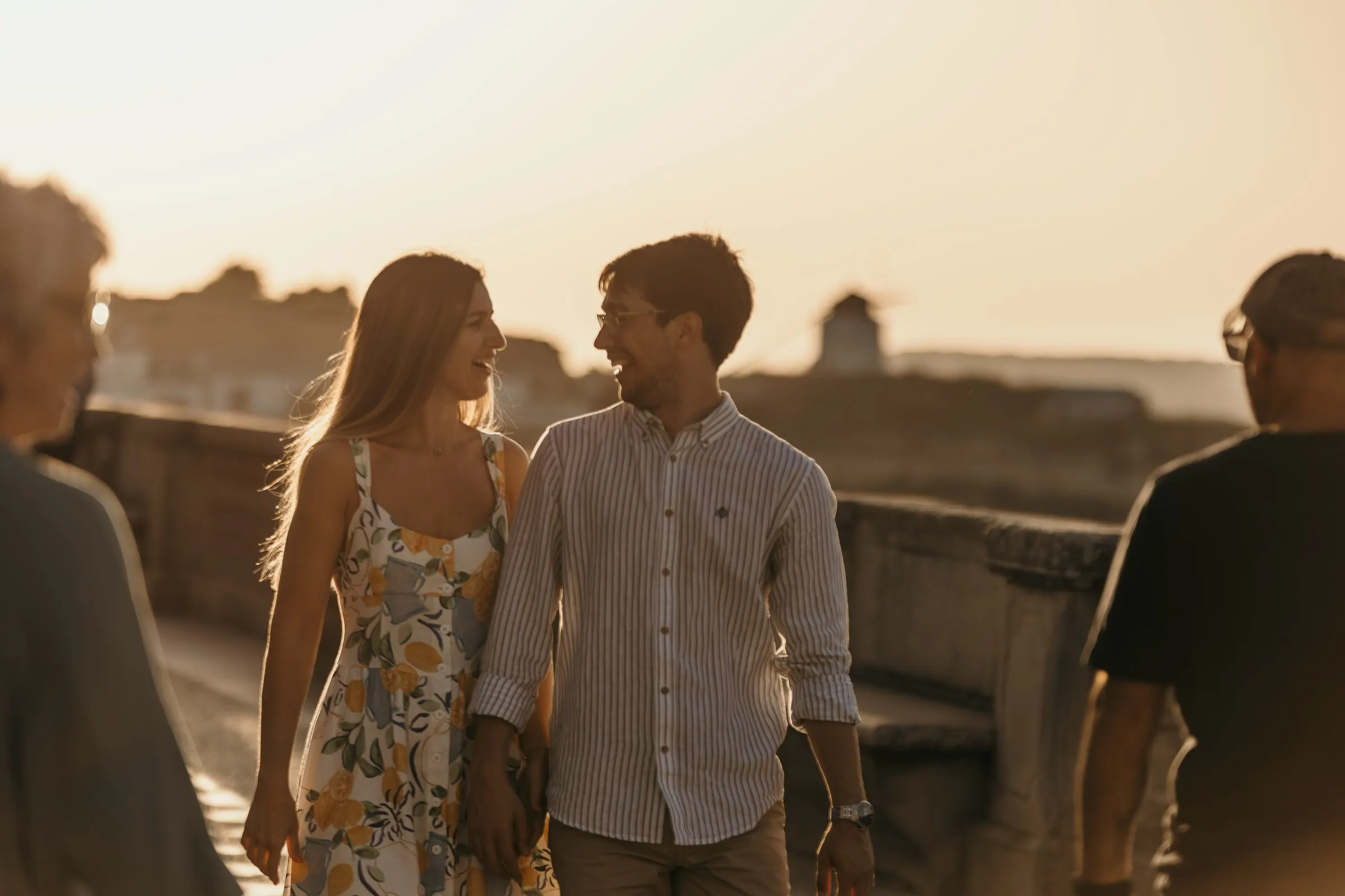 La pareja ríe en el paseo al atardecer en Vejer, enmarcada por paseantes en primer plano