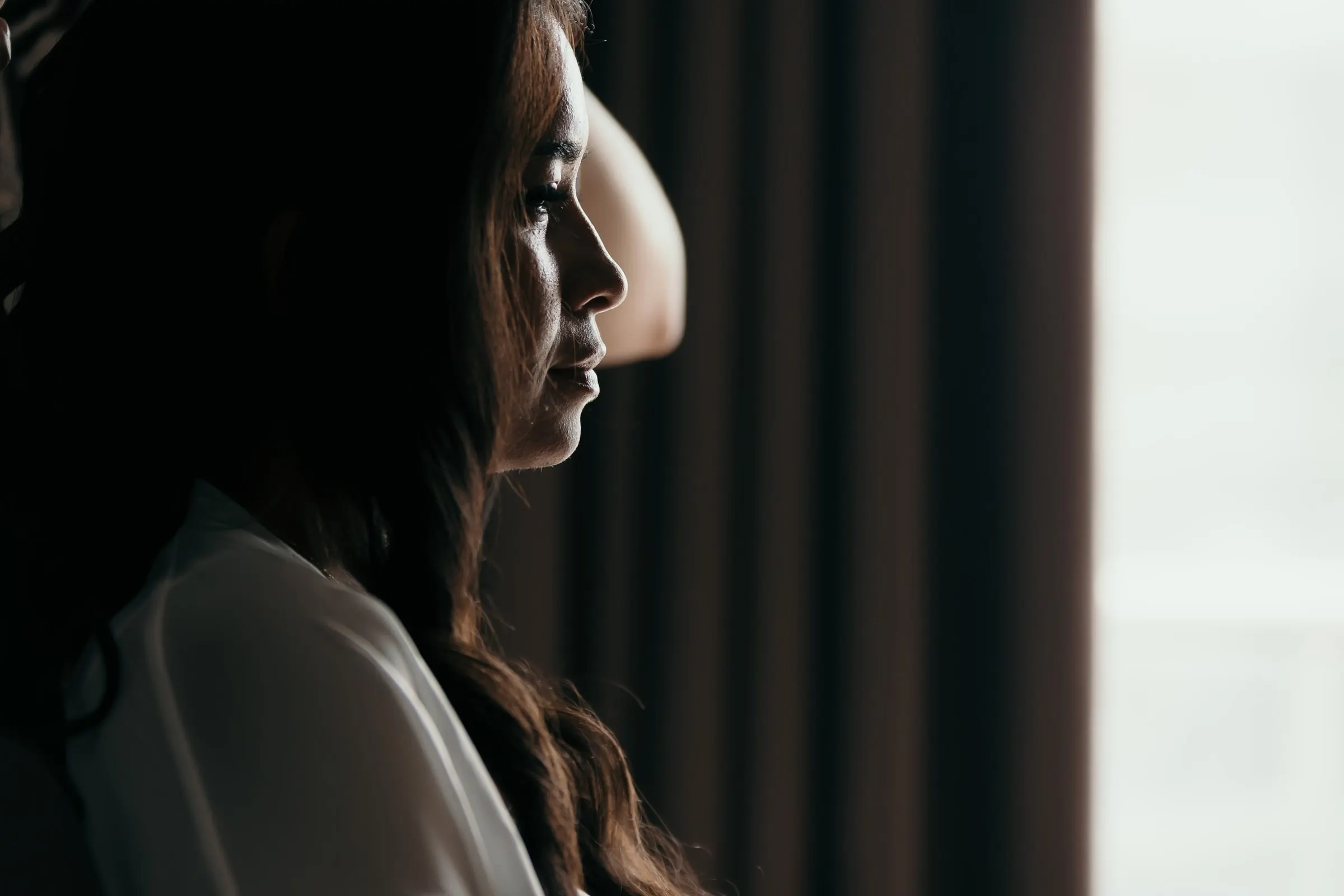 Bride in profile in the half-light beside a dark curtain before her Marbella wedding