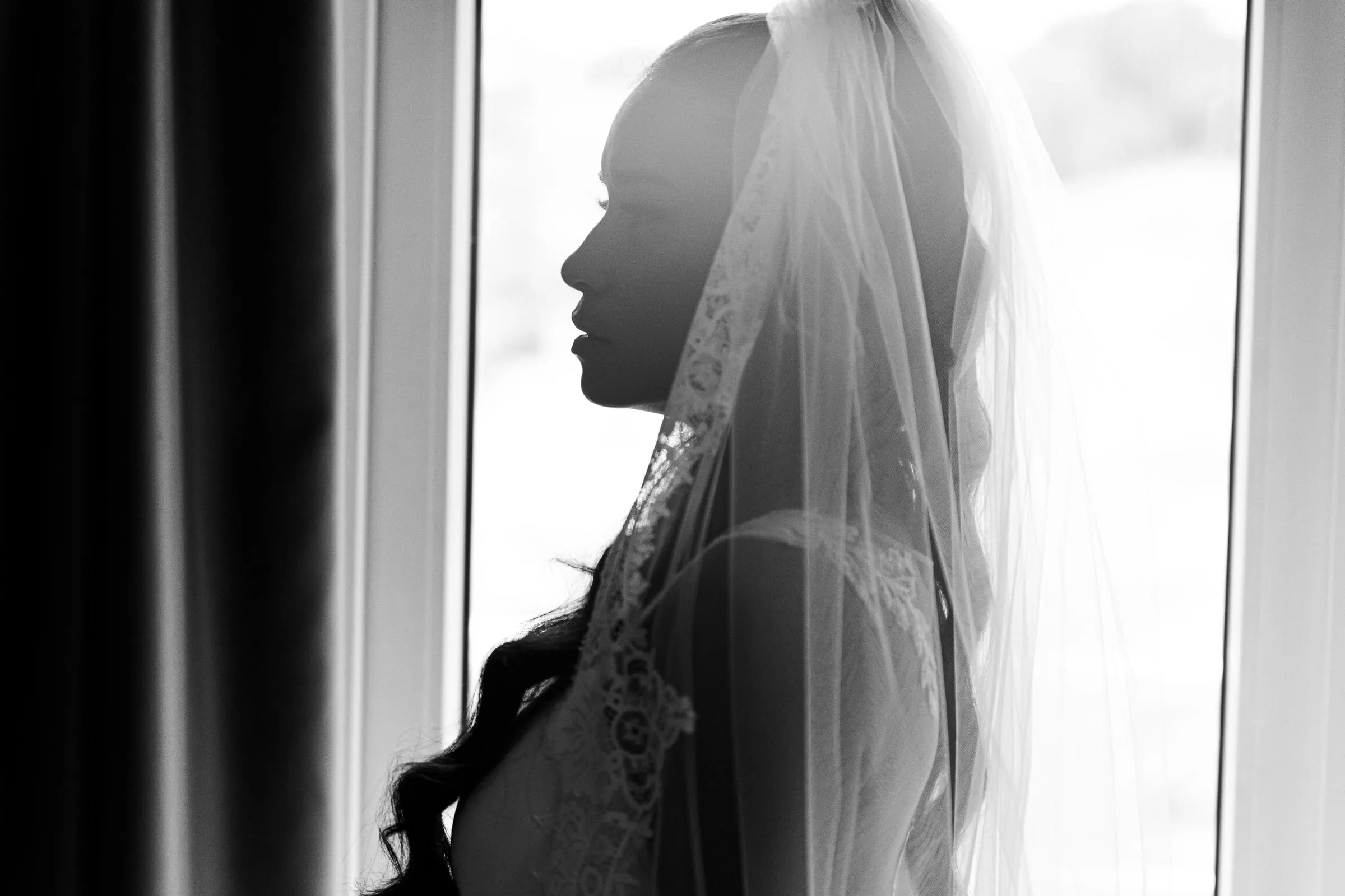 Black and white silhouette of the bride under her lace veil against the window light