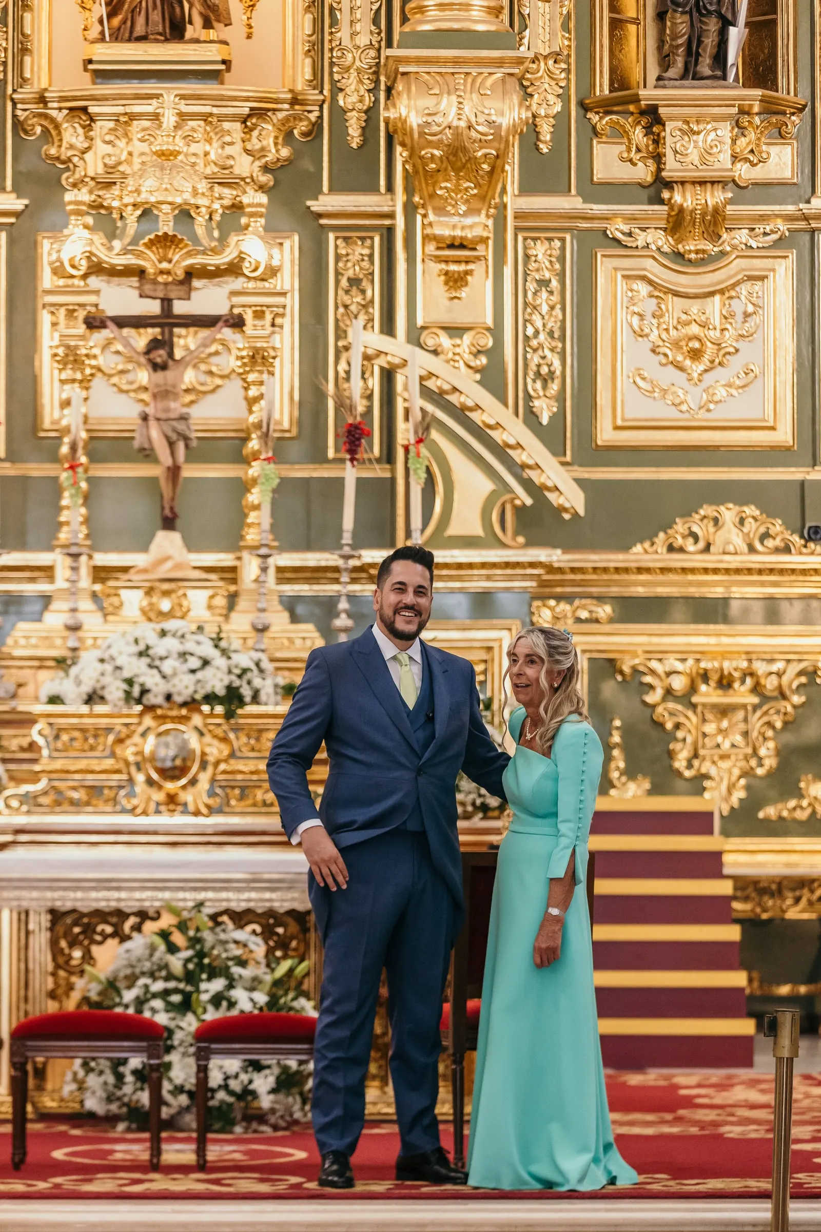 Groom and his mother waiting at the altar in front of the gilded green and gold altarpiece