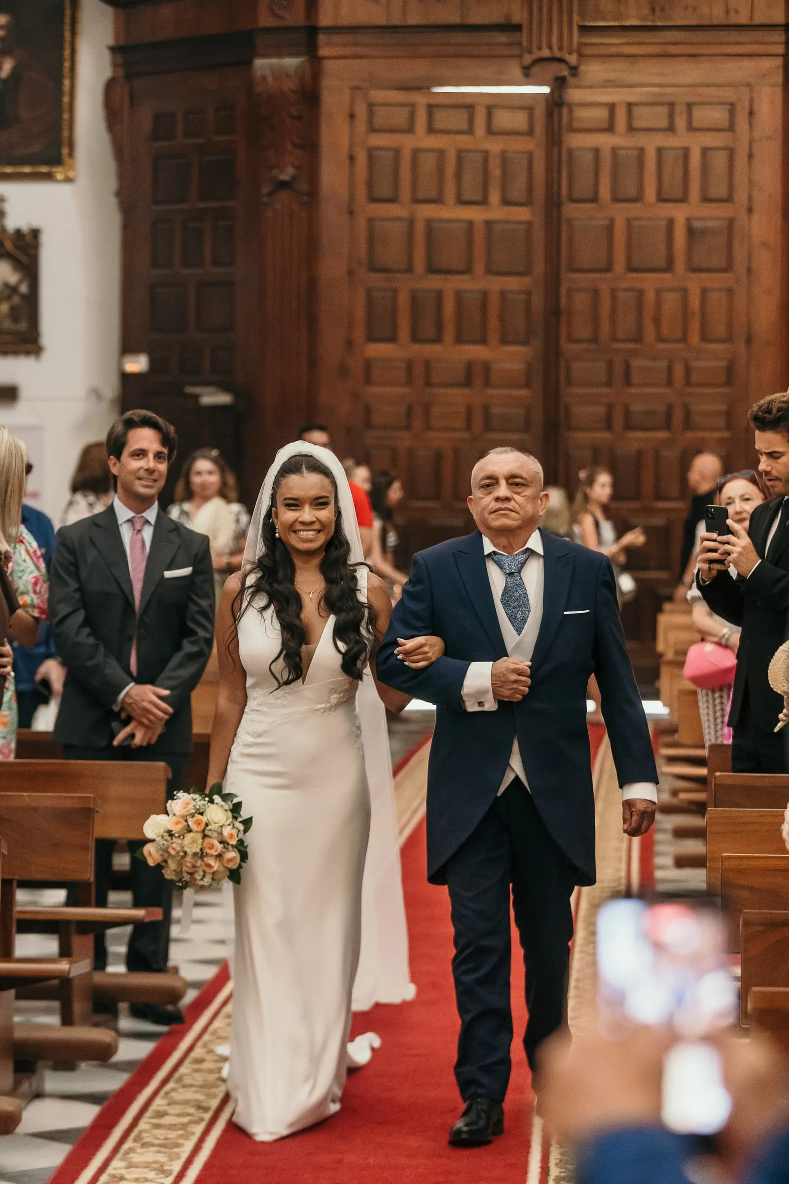 Bride walking down the red carpet on her father's arm as guests take photos, Marbella church wedding