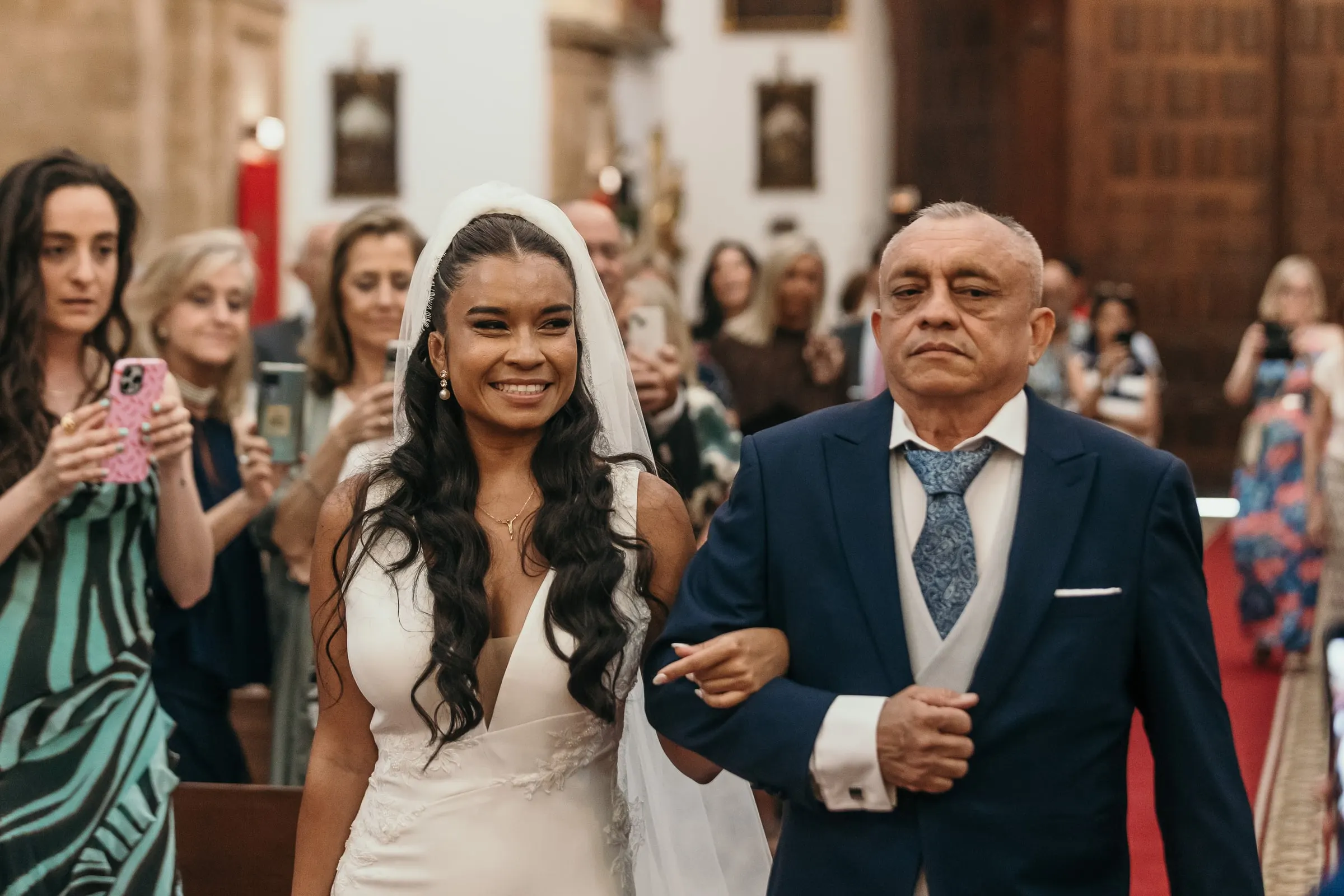 Bride smiling at her father as they walk up the aisle between the guests