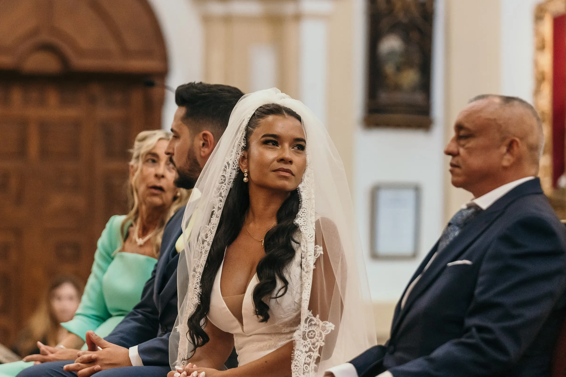 Bride seated beside the groom during the ceremony, looking up towards the altar