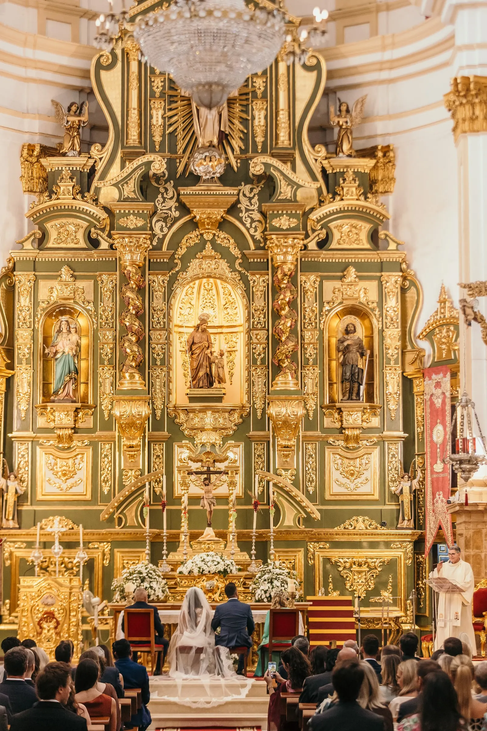 Wide view of the baroque gold altarpiece with the couple at the altar during the church ceremony in Marbella