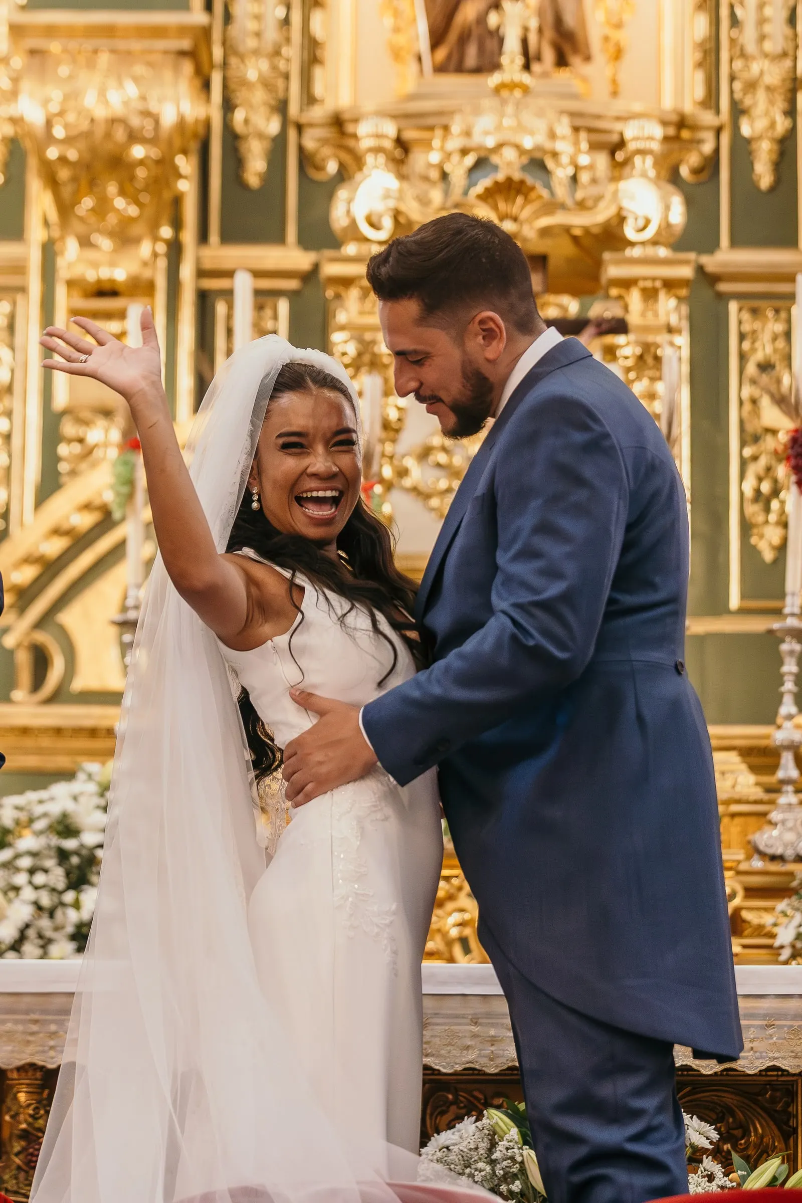 Bride raising her arm and laughing as the groom hugs her at the altar