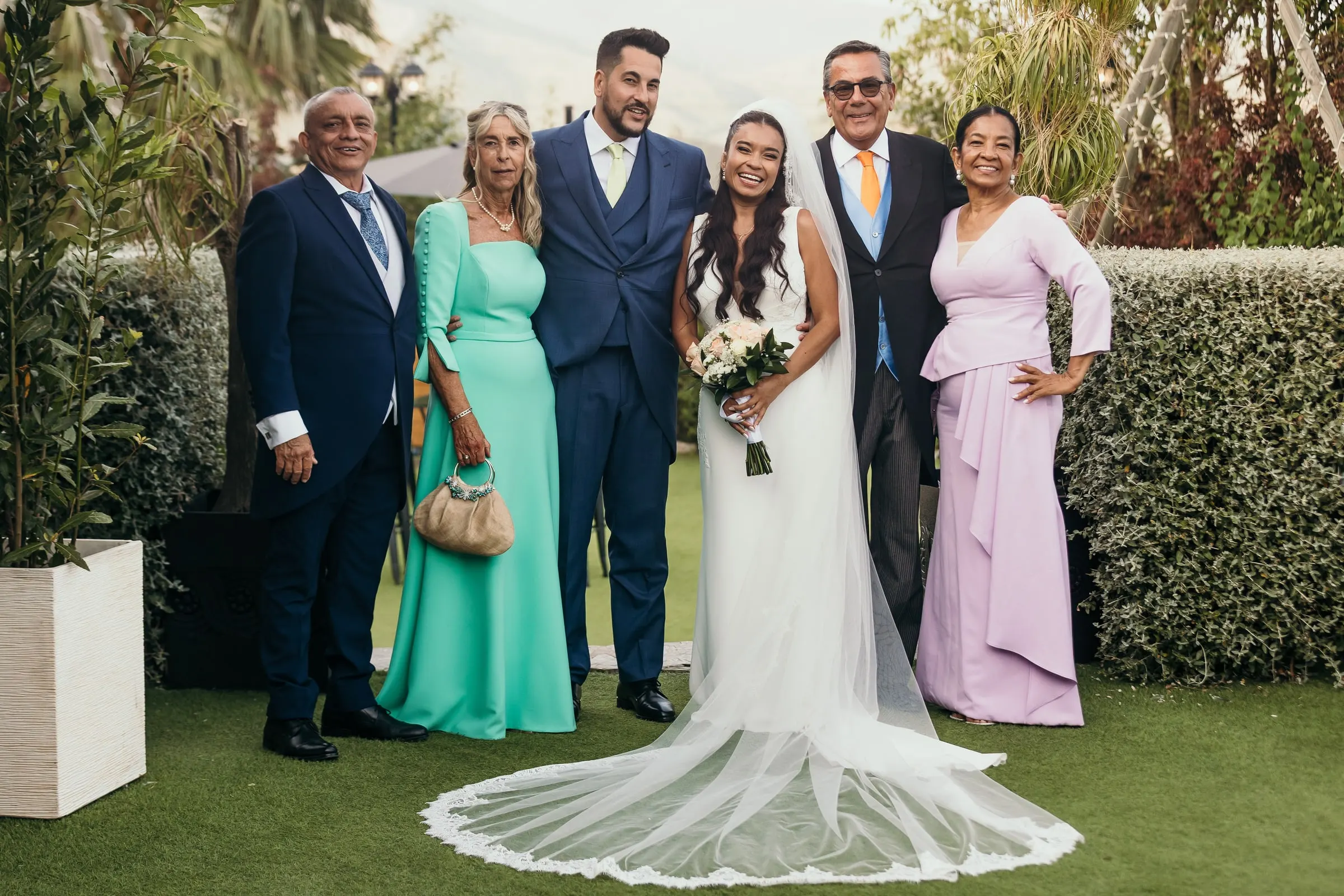 Family portrait with both sets of parents on the lawn, the bride's long veil spread across the grass