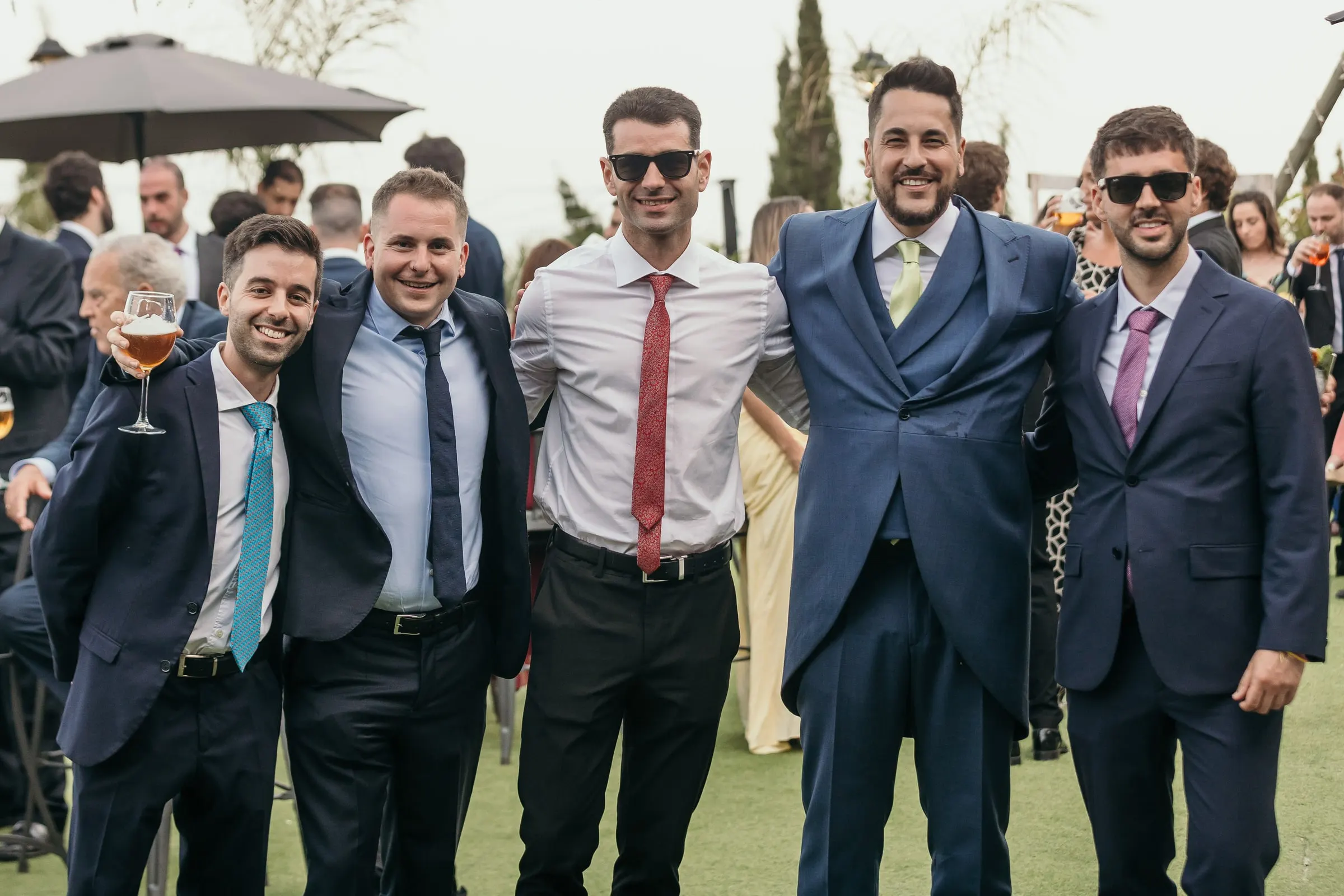 Groom with his friends, some in sunglasses, posing on the lawn at the cocktail hour