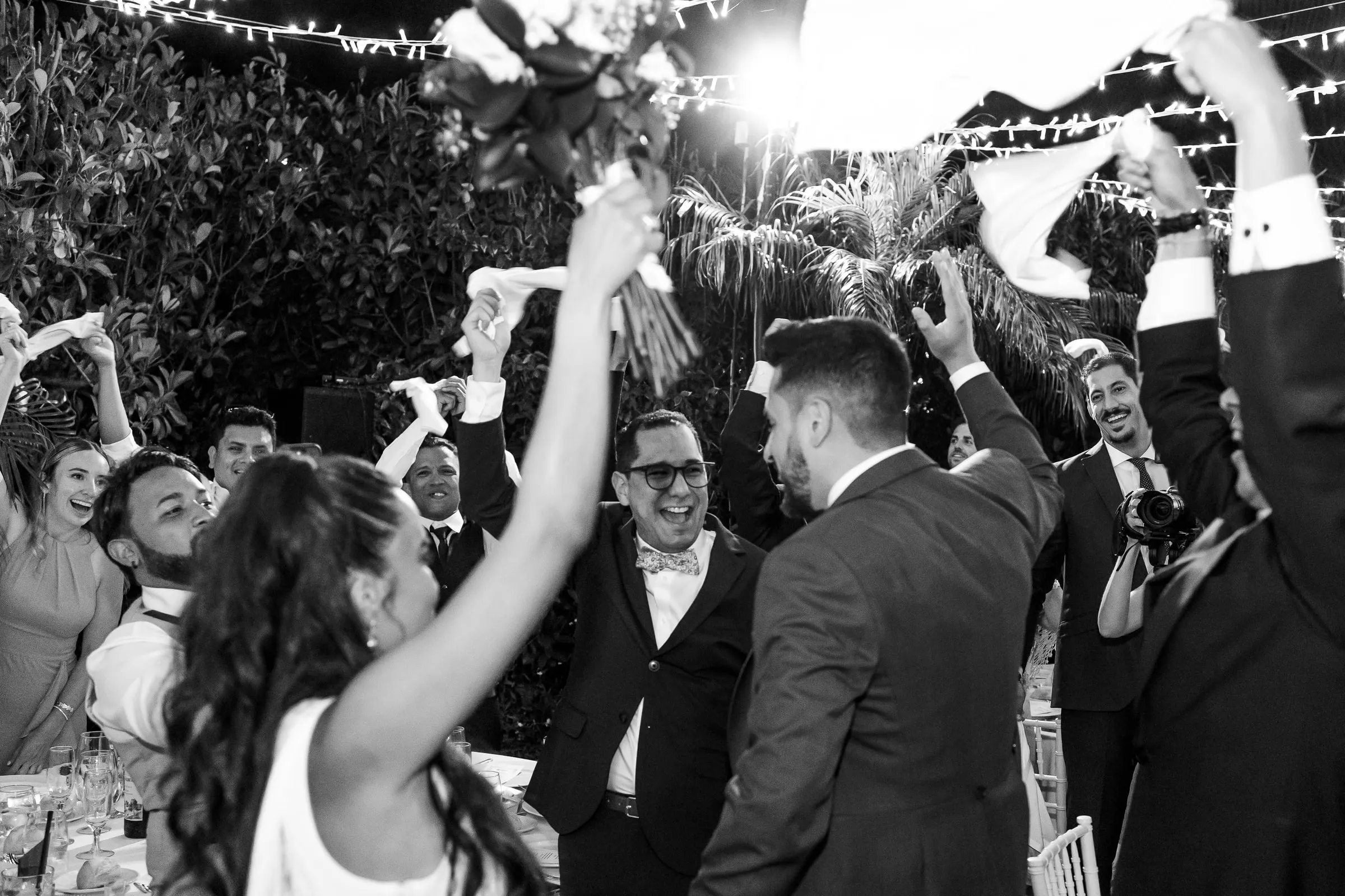 Black and white photo of the bride throwing her bouquet in the air amid waving napkins