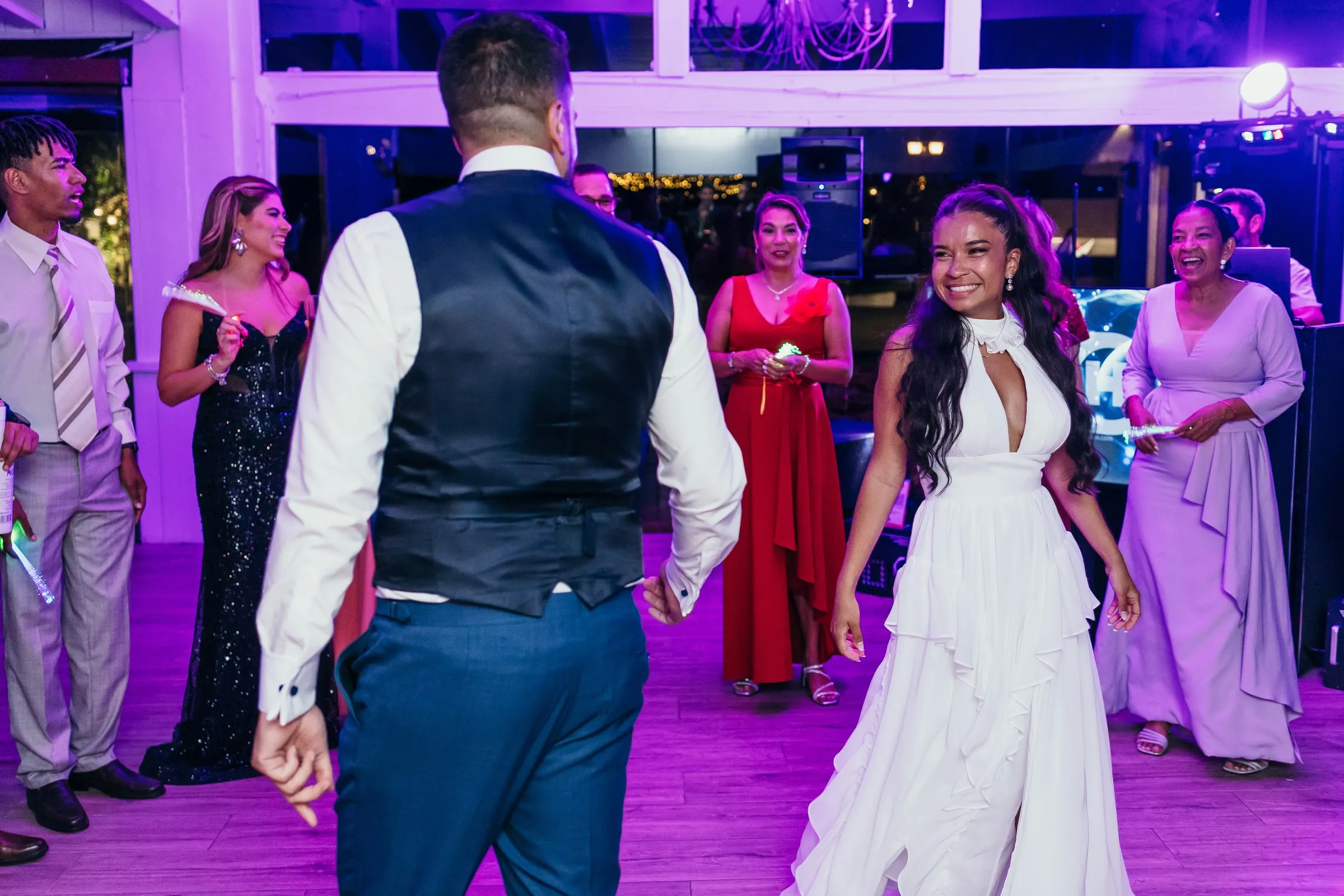 Bride dancing towards the groom on a dance floor lit in purple
