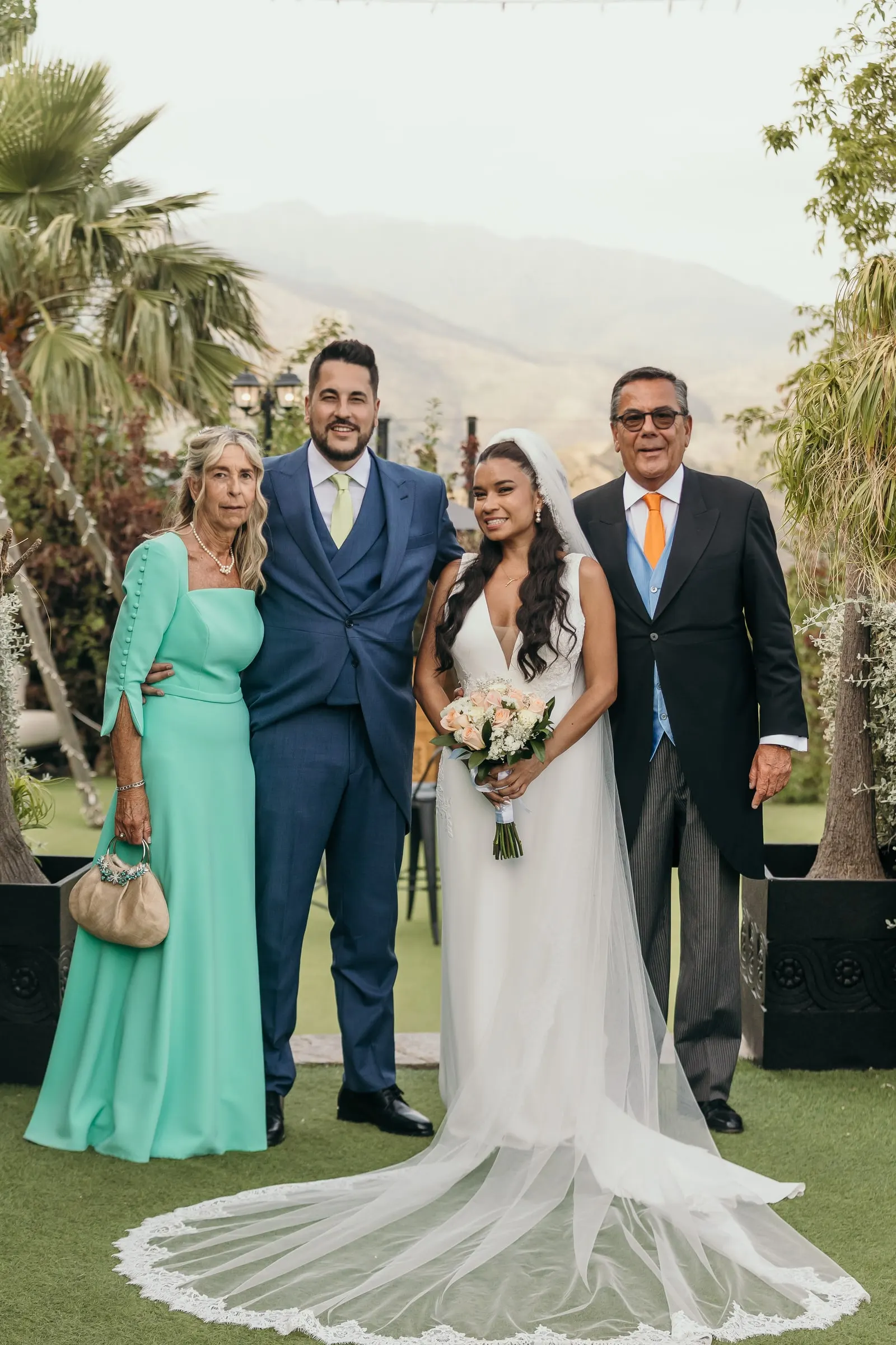 Newlyweds with the groom's parents on the lawn under the palm trees, the hills of Marbella behind
